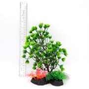 A plastic model of a green aquarium plant with pink and green foliage at the base, placed beside a transparent ruler showing the plant is about 18 centimeters tall.