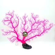 A bright pink artificial coral decoration with branching patterns stands upright on a black base. A ruler and a small round label are attached to the coral for size reference. The background is plain white.
