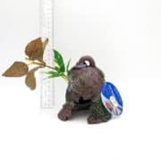 A decorative aquarium ornament shaped like a turtle with artificial plants attached, placed next to a transparent ruler for scale. The ornament has a blue tag and is set against a white background.