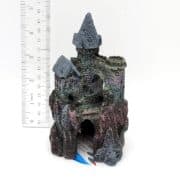 A small, detailed model of a stone castle with two towers and an arched entrance, placed next to a ruler for scale. The castle is about 12 cm tall and appears to be made of textured, painted material.
