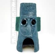 A blue, textured, stone-like ornament resembling a face with circular eyes and an open mouth stands upright; a ruler beside it shows it is about 15 cm tall.