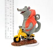 A figurine of a gray rat wearing an orange vest rides a small yellow scooter on a brown base. A ruler beside the figure shows its height is about 4 inches. The background is plain white.