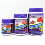 Three OCEAN NUTRITION PRIME REEF FLAKES containers, with purple lids and tropical fish images, come in various sizes. Perfectly formulated for all tropical species, they provide premium nutrition for your aquatic companions.