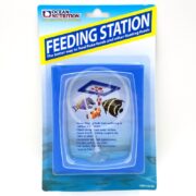 The OCEAN NUTRITION FEEDING STATION packaging showcases a blue-bordered holder with vibrant fish and flake food illustrations. Text emphasizes benefits like waste reduction and keeping food afloat. Enhance your aquarium feeding experience with item #25125.