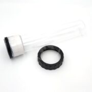 A transparent cylindrical plastic tube, resembling a PondMax Pressure Filter Replacement Quartz Sleeve, with a black cap rests on a white surface. Beside it lies a separate black ring-like component. The tube is designed with a sleek white base accented by a subtle black rim.