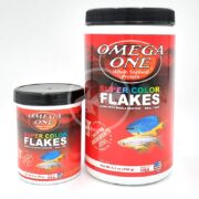 Two OMEGA ONE SUPER COLOR FLAKE fish food containers are shown, the larger to the right and smaller to the left, both featuring vibrant red packaging with fish images and labeled Made with Whole Seafood, Meal-Free..