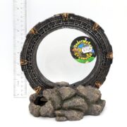 The UT RESIN SUNKEN METALLION LG 8 is a decorative circular resin model resembling a stargate, featuring detailed carvings and placed on a rocky base. It evokes underwater treasures, stands about 10 inches tall, and is priced at $29.99, with a ruler beside it for scale.
