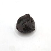 A single dark brown, round ball of tamarind paste on a white background.