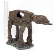 The UT RESIN SPACE BATTLE TANK LG features a four-legged, machine-like armored design on a rocky base. It has detailed resin legs, a mounted head, and measures about as tall as the ruler beside it. A hollow section is visible on one side.