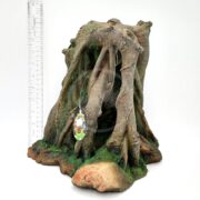 The UT RESIN MANGROVE CAVE is a realistic tree stump aquarium decor, crafted from durable resin with twisted roots and moss accents mimicking a mangrove cave. Its brown with green highlights, includes a small tag, and is displayed beside a ruler for height reference.