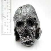 The UT RESIN MASK RUIN is a metallic skull sculpture with exaggerated features, dark hollow eye sockets, and a weathered texture. It sits beside a ruler that indicates its height as approximately 3 inches, evoking the look of underwater treasures.