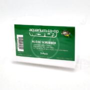 A package labeled aquarium co-op ALGAE SCRUBBER contains three white scrubber pads for cleaning aquarium tanks, with green and white text highlighting features and usage instructions.