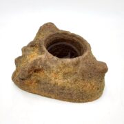 A rough, brown, rock-like object with an open circular hollow at the top, resembling a rustic container or planter, set against a plain white background.