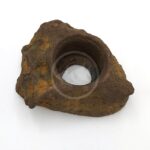 A rough, brown, rock-shaped object with a hollow circular center, resembling a natural stone or possibly an artificial decorative item, set against a plain white background.