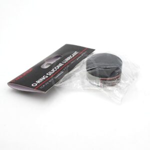 A 1.5 oz black AQUATOP O RING SILICONE LUBRICANT, partially wrapped in clear plastic, sits next to its black and red label packaging on a white surface.