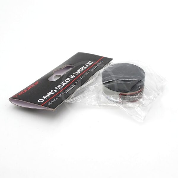 A 1.5 oz black AQUATOP O RING SILICONE LUBRICANT, partially wrapped in clear plastic, sits next to its black and red label packaging on a white surface.