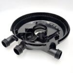 A black circular plastic mechanical part with two threaded pipe connectors protruding from the side, set against a plain white background. The part has internal compartments and ridged detailing along the edge.