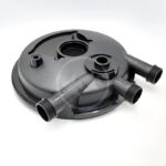 A black circular plastic component with three threaded pipe connectors extending from its side, placed on a white background. The part has multiple openings and raised areas, suggesting it is used in plumbing or machinery.