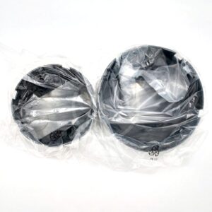 Two black circular objects wrapped in clear plastic, placed side by side on a white background. The objects differ in size, with the one on the right being larger. Recycling symbols are visible on the plastic.