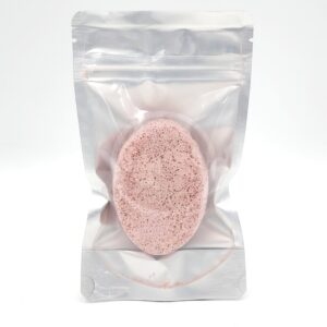 A pink oval sponge is sealed inside a clear, resealable plastic pouch standing upright against a white background.