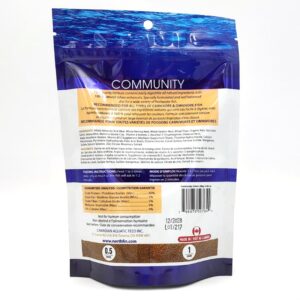 Back view of a blue and white bag of fish food labeled COMMUNITY, showing feeding instructions, ingredients, guaranteed analysis, barcode, and a Made in the USA logo at the bottom.