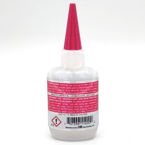 A white bottle with a pink pointed cap, featuring warning labels and instructions in red and black text. The label includes hazard symbols and a barcode at the bottom. The product appears to be an adhesive or glue.