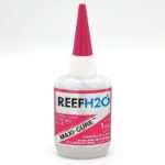 A bottle of REEF H2O Maxi-Cure extra thick glue with a pink cap and label, showing it contains 1 oz (28g) of cyanoacrylate adhesive and warning of eye and respiratory irritation.