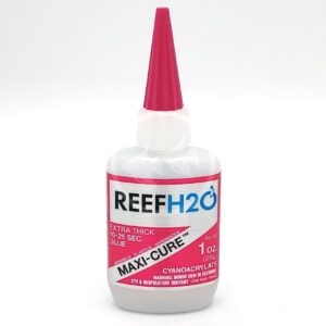 A bottle of REEF H2O Maxi-Cure extra thick glue with a pink cap and label, showing it contains 1 oz (28g) of cyanoacrylate adhesive and warning of eye and respiratory irritation.