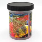 A plastic jar of fish food with a black lid, featuring colorful fish images and detailed nutritional information and ingredients printed on a label. The jar is marked 10 oz 283 grams at the bottom.
