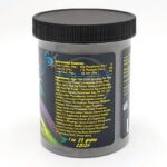 A black container with a screw-on lid displays a yellow label listing the guaranteed analysis, ingredients, and product weight (1 oz, 28 grams). Colorful fish graphics are visible on the left side of the container.