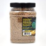 A clear plastic jar with a black lid filled with brown pellet fish food. The label on the jar features feeding instructions, product information, a green fish image, a goldfish image, and a small USA flag icon.