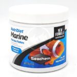 A white container of Seachem NutriDiet Marine Flakes fish food, featuring an image of a clownfish, product branding, and labels highlighting probiotics formula and suitability for all marine fish.