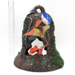 The PP RESIN SUNKEN GARDENS BELL is a decorative, hollow ornament shaped like a mossy tree stump with artificial orange and yellow leaves, standing about 9 inches tall.