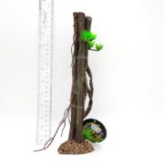 The UT RESIN MINI MANGROVE ROOT PLANT B features two brown tree trunk decorations with green artificial plants and a circular black tag, shown next to a 12-inch ruler for scale on a white background.