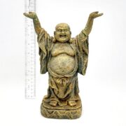The PP RESIN STANDING BUDDHA RR682 is a small, weathered resin statue featuring a smiling, bald Buddha with arms raised and wearing a robe. A ruler beside it indicates its height is approximately 15 centimeters.