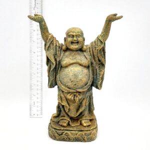The PP RESIN STANDING BUDDHA RR682 is a small, weathered resin statue featuring a smiling, bald Buddha with arms raised and wearing a robe. A ruler beside it indicates its height is approximately 15 centimeters.