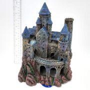 The PP RESIN WIZARDS CASTLE LG RRW8 features blue conical roofs and arched doorways atop textured rock. Standing about 20 cm tall, this large resin castle is shown beside a ruler on a plain white background.