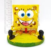 The PP RESIN SPONGEBOB W SWIM THROUGH HOLES 5 IN is a resin SpongeBob figurine on a yellow-green base, smiling and giving a thumbs up, with swim-through holes and stands about 5 inches tall.