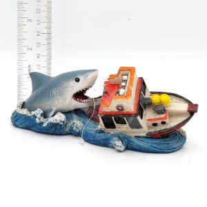 The PP RESIN JAWS BOAT ATTACK SMALL JWSR4W features a small fishing boat attacked by a jaws-style shark leaping from ocean waves, mouth open near the stern. A ruler behind the figurine provides scale.