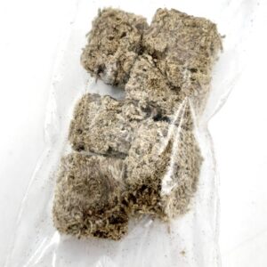Six beige, fibrous rectangular blocks are packed together inside a transparent plastic bag on a white background. The blocks appear dry and textured, resembling compressed plant or fiber material.