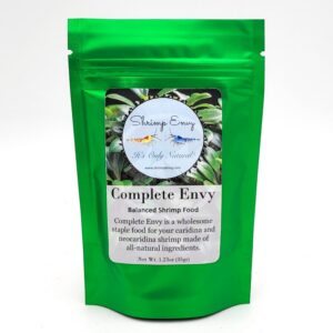 A shiny green pouch labeled Complete Envy Balanced Shrimp Food by Shrimp Envy, featuring a circular logo with shrimp images and text describing it as a wholesome staple food for aquarium shrimp.