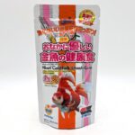 A silver and white package of Hikari Goldfish Wheat-Germ fish food with Japanese text, an image of a goldfish, and colorful labels. The package is upright with a resealable top.